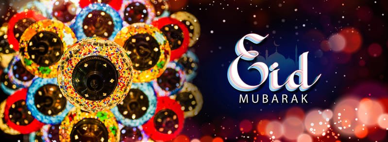 Bannière festive divisée en deux parties. À gauche, un gros plan vibrant sur de multiples lampes turques en mosaïque de verre coloré (rouge, bleu, jaune, orange) suspendues au plafond, créant un motif kaléidoscopique lumineux. À droite, sur un fond bleu nuit parsemé d'étoiles et de bokeh lumineux rouges, le texte "Eid Mubarak" est écrit en calligraphie blanche élégante avec des touches de bleu et de rose, surmonté de la silhouette subtile d'une mosquée et d'un croissant de lune