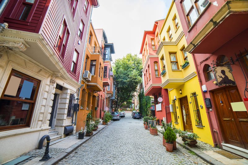 Je marche dans une ruelle de Balat à Istanbul, quartier pittoresque aux maisons ottomanes colorées en rose, jaune et orange, avec des façades restaurées, balcons en bois et pavés anciens.