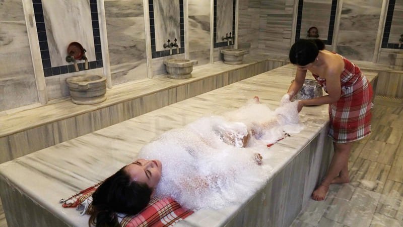 Femme allongée sur le marbre d'un hammam à Istanbul recevant un massage savonneux traditionnel au bain turc